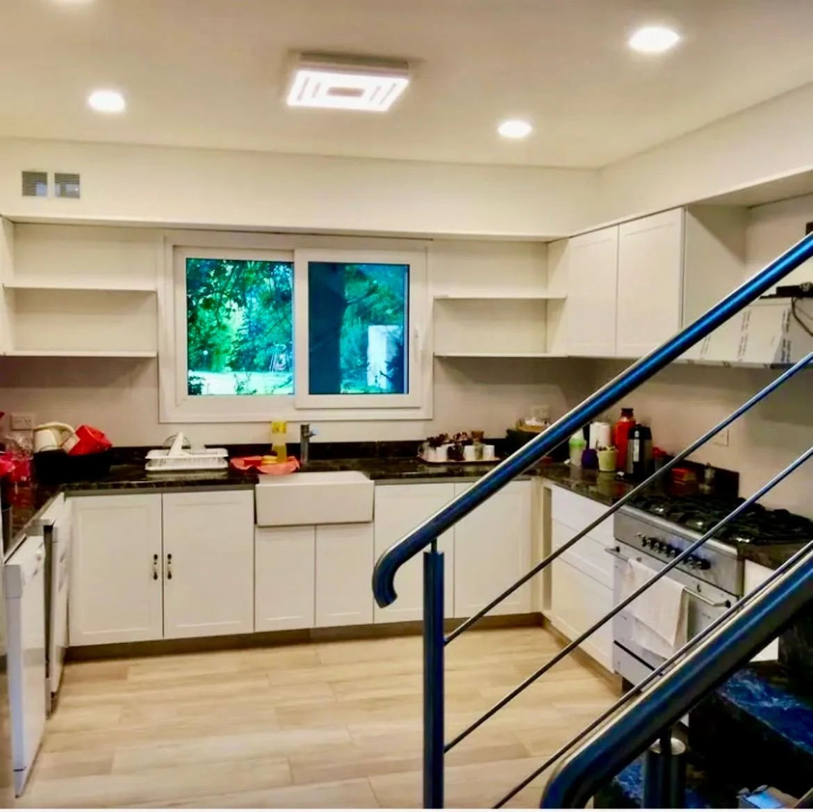 Cocina blanca abierta al ambiente con estantes junto a la ventana