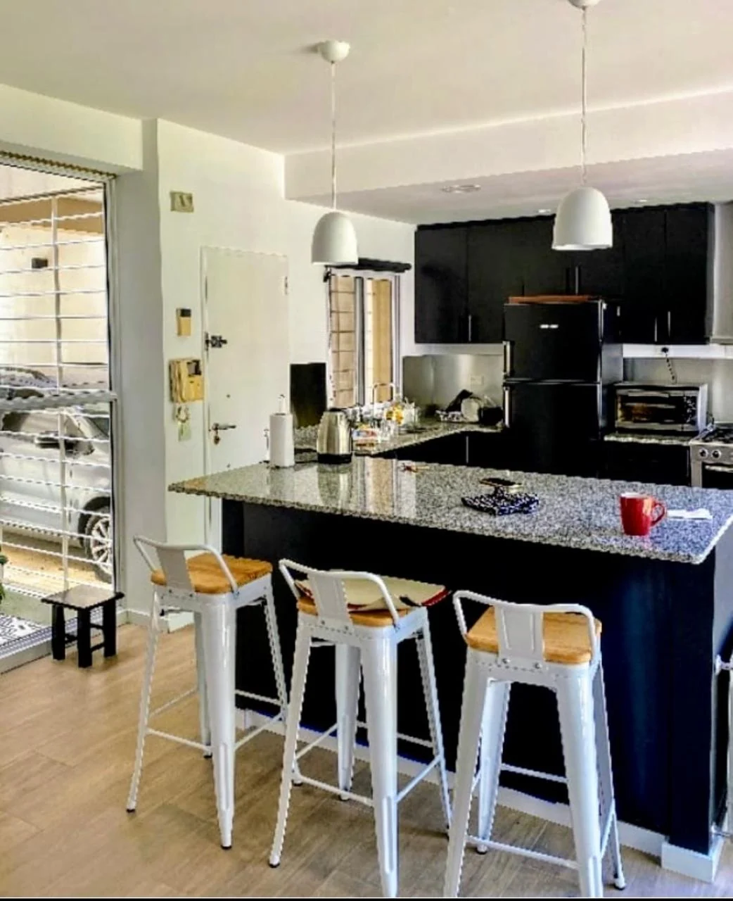 Cocina con muebles oscuros e isla central acompañada por tres banquetas blancas