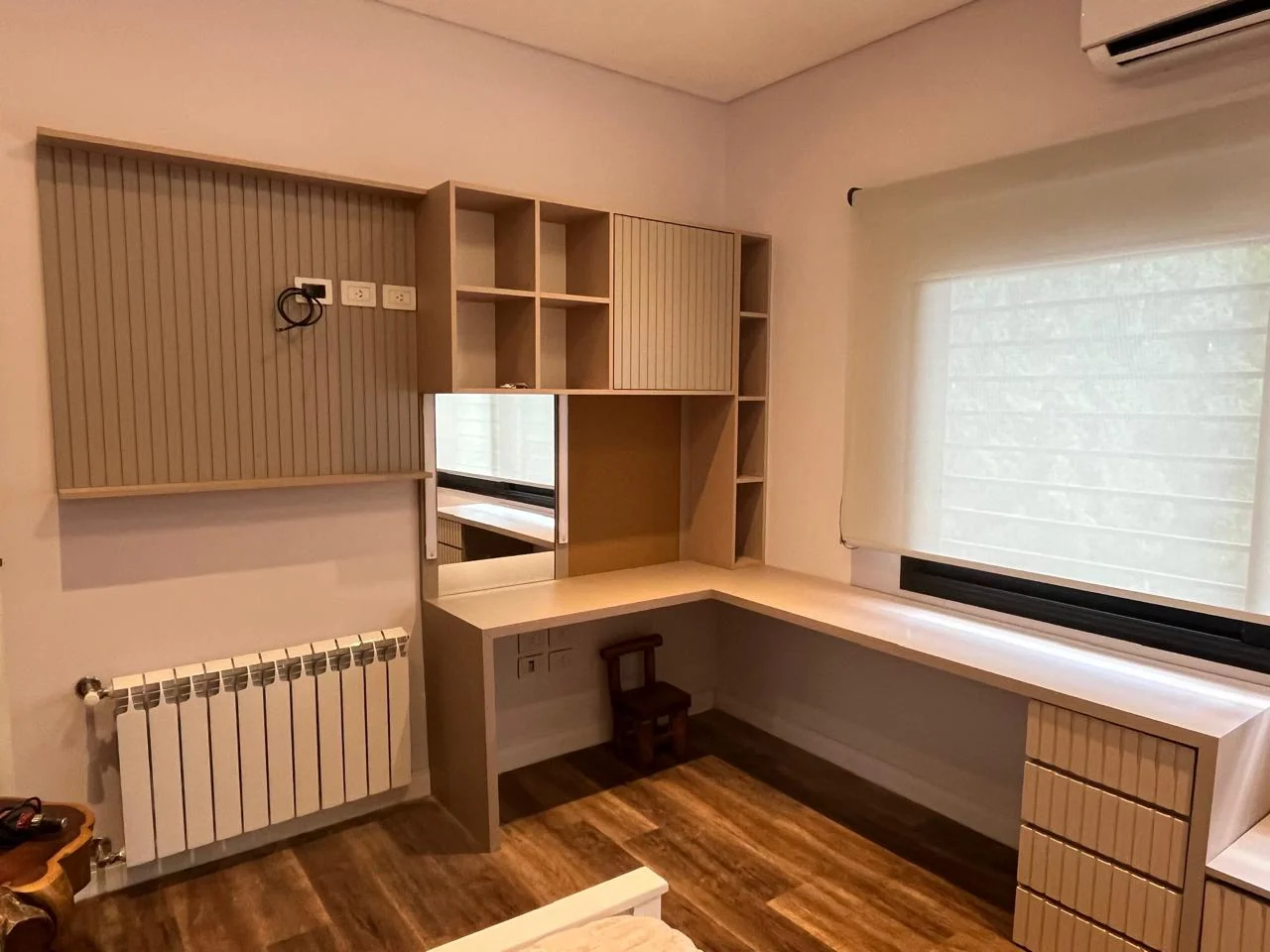 Escritorio en esquina junto a una ventana, con estantes y cajonera de frentes ranurados